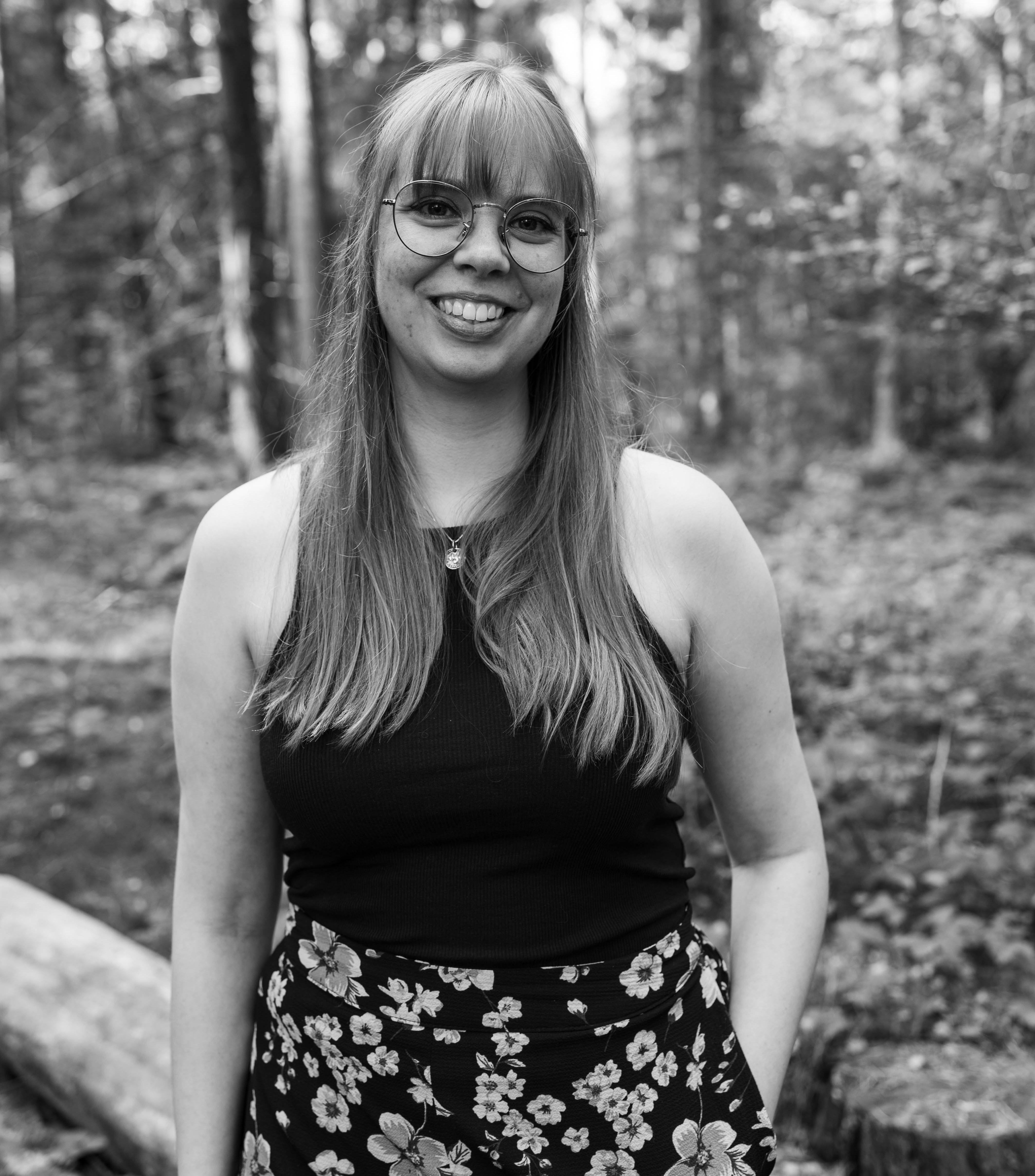 Portret of Rachèl van Dijkhorst standing in a forest and smiling.